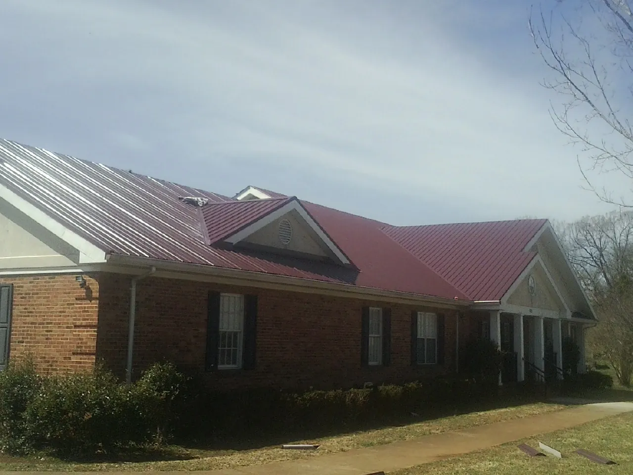 Red metal roof with gabled entries on a long brick building, from a Hail Damage Roof Repair job in Ball Ground