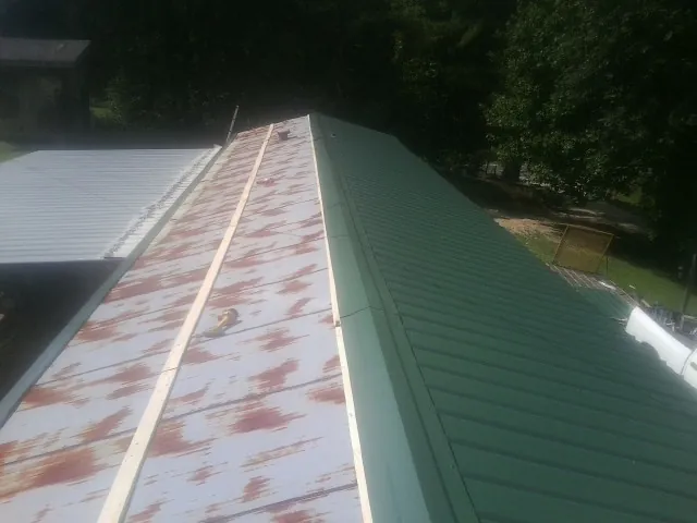 Old rusted panels beside newly installed green metal roofing — Wind Damage Roof Repair by Roofing Brothers in Ball Ground