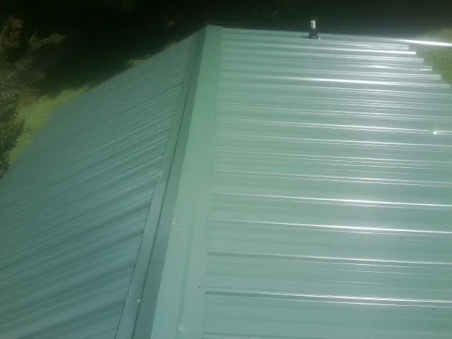 New green metal panels meeting at the ridge of a roof — Flat Roof Repair work by our crew in Ball Ground
