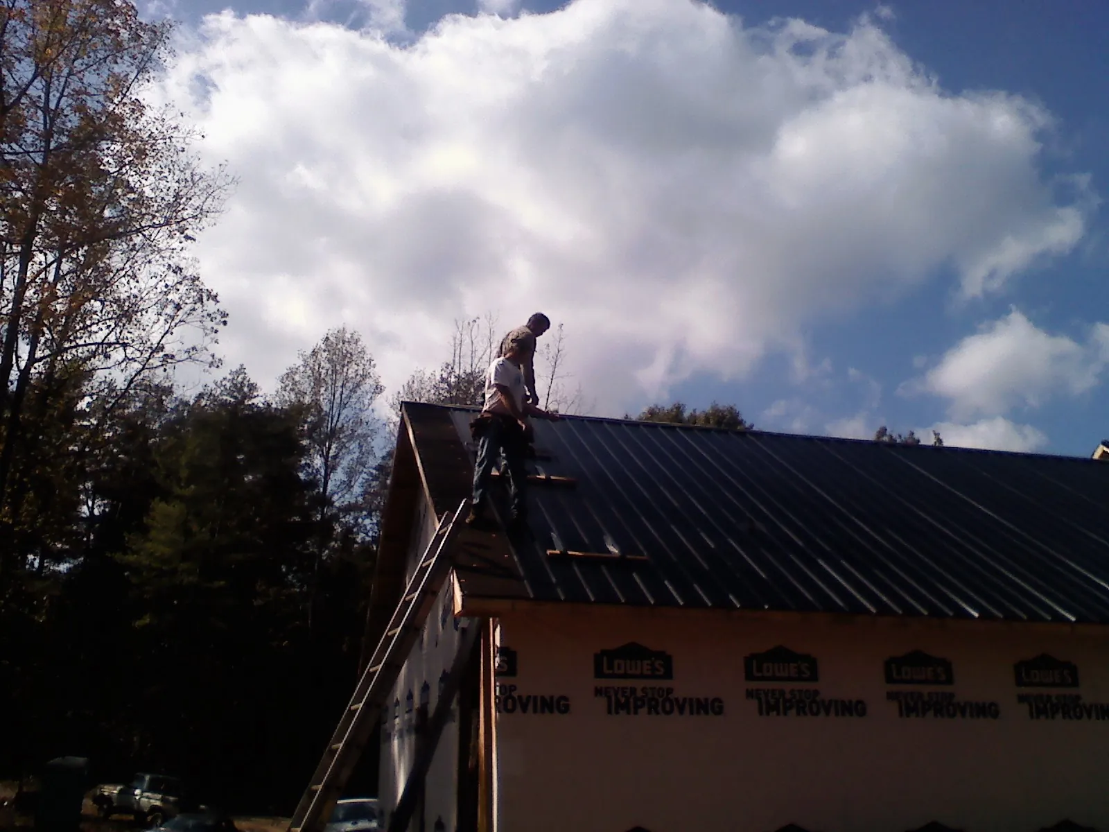 Roofer fastening dark metal panels high against a cloudy sky, from a Roof Inspection job in Ball Ground