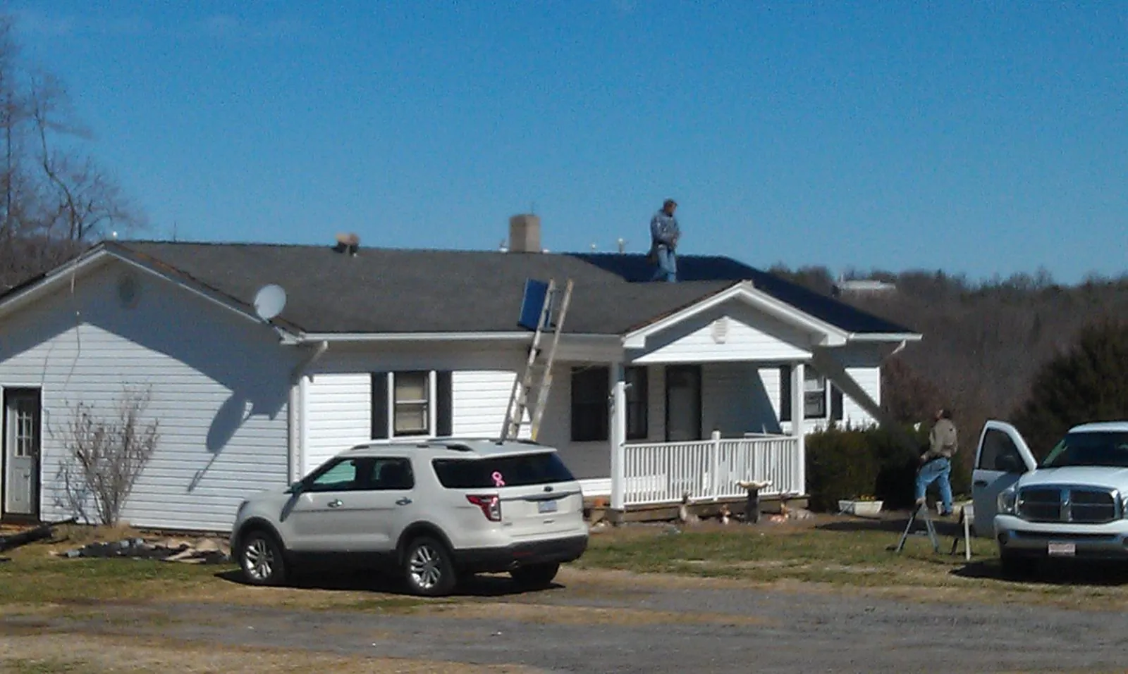 Roofers stripping shingles from a white ranch house roof in Ball Ground