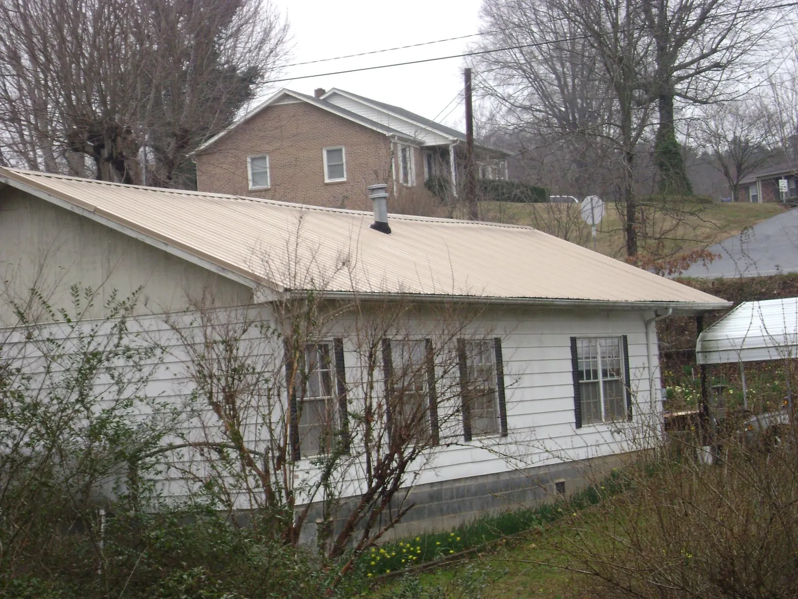 Tan metal roof on a white sided house set into a hillside — Commercial Roofing by Roofing Brothers in Ball Ground