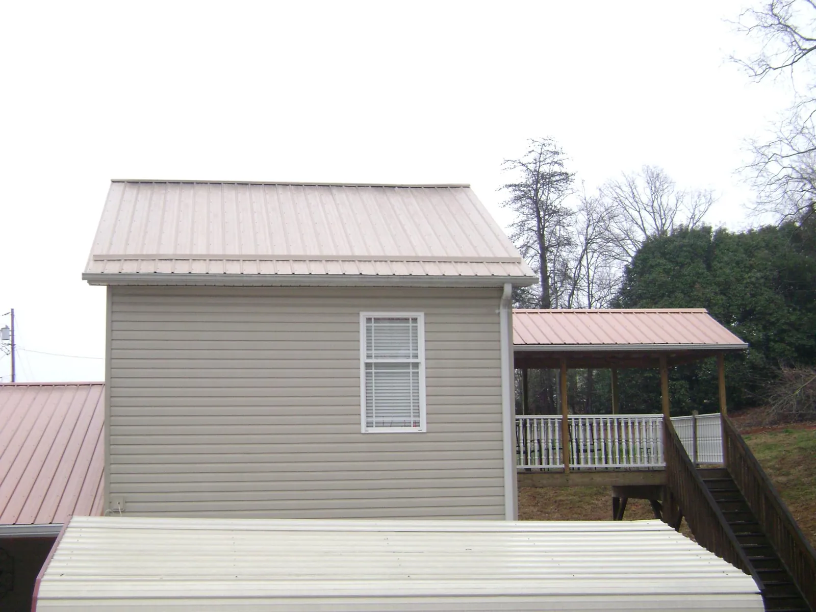Tan metal roofs on a two story addition and attached porch, from a Roof Replacement job in Ball Ground